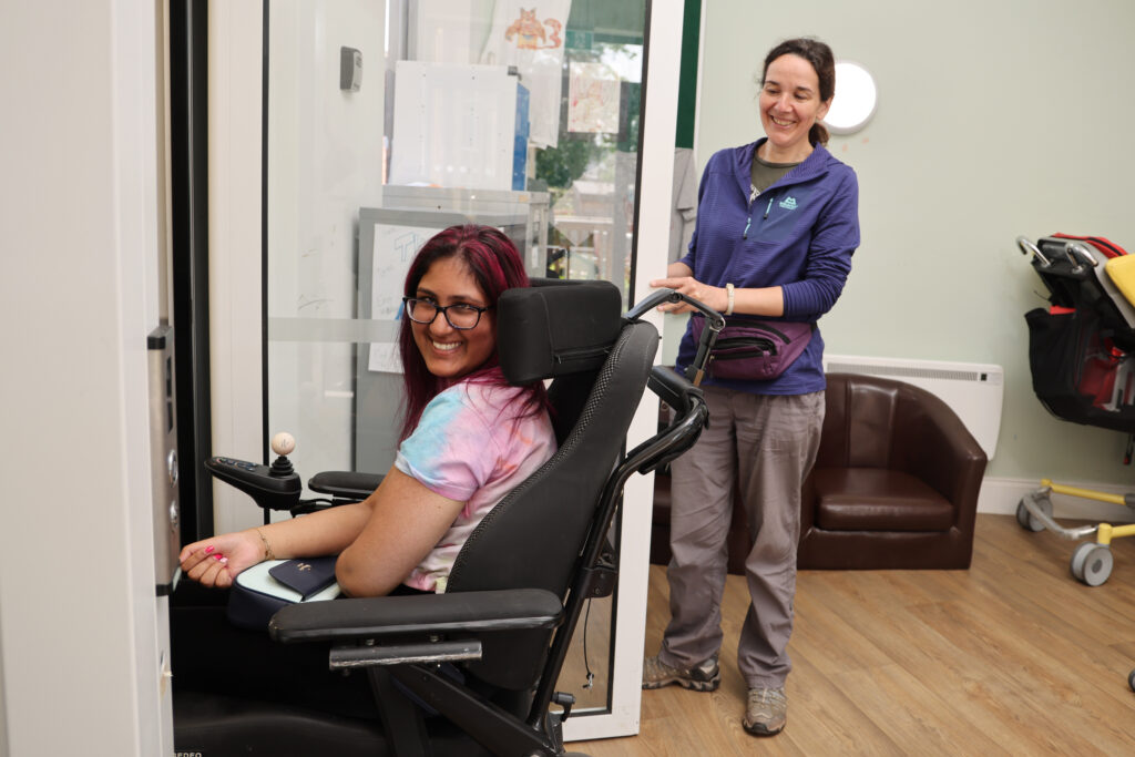 Female student in wheelchair smiling next to care and support worker