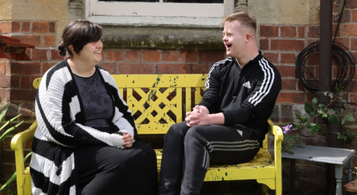 Students Holly and Josh smiling sat outside on a bench